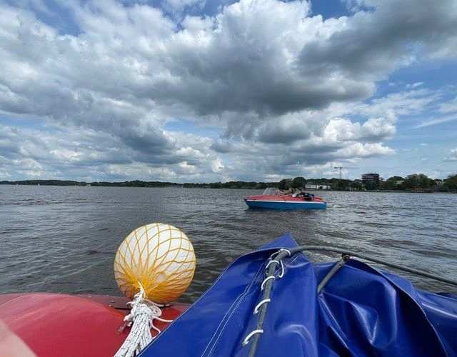 Blick von einem Boot mit Boje auf ein anderes Boot auf einem großen See unter bewölktem Himmel.