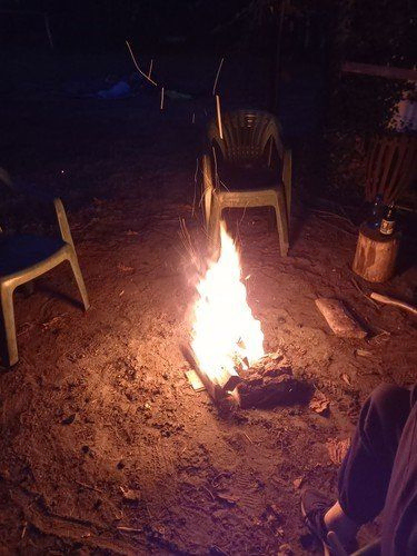 Ein Lagerfeuer brennt nachts hell auf dem Boden, umgeben von Stühlen.