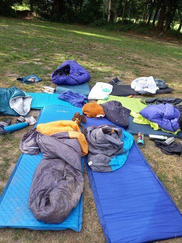 Schlafsäcke und Matten auf Gras für ein Campinglager ausgebreitet.