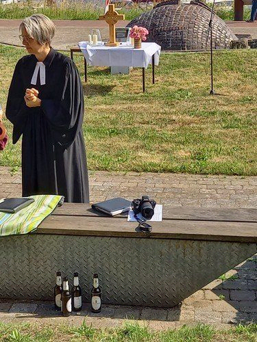 Eine Person in Geistlichenkleidung steht draußen bei einem Altar mit Kreuz und Blumen.